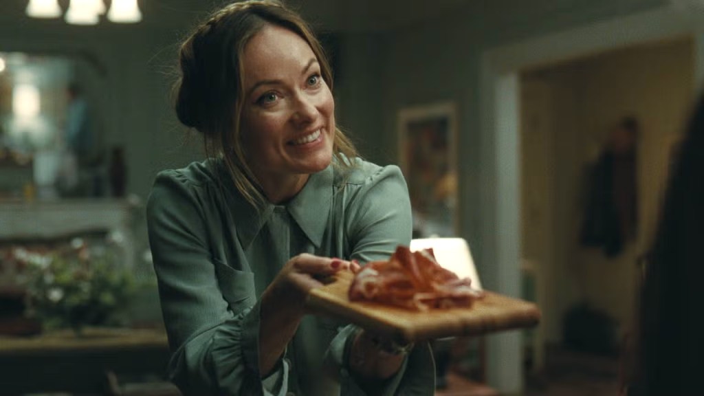 Oliva Wilde presents snacks with a fake smile.